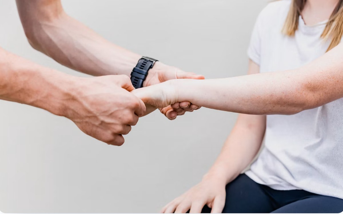 A therapist supporting a seated patient’s arm through a range-of-motion exercise.
