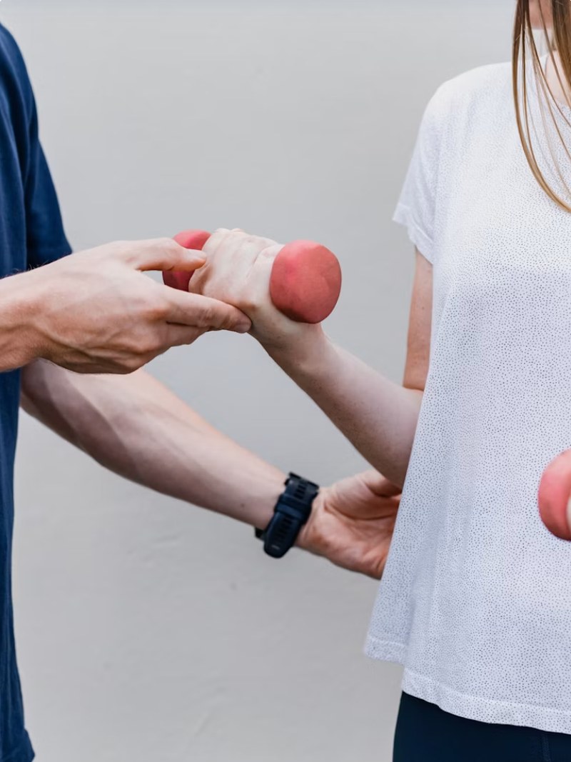 A therapist guiding a patient through a dumbbell exercise.