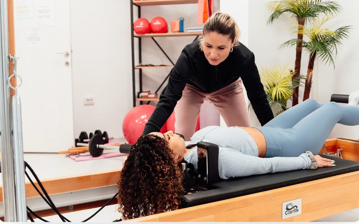 A therapist supervising a patient on a reformer in a rehabilitation studio.